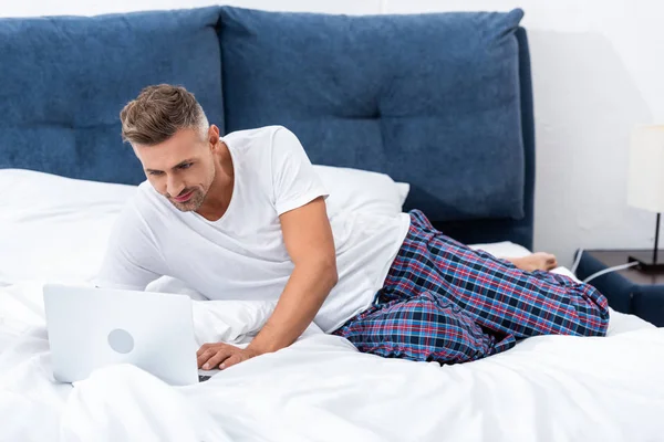 Freelancer adulto feliz deitado na cama e usando laptop durante o horário da manhã em casa — Fotografia de Stock