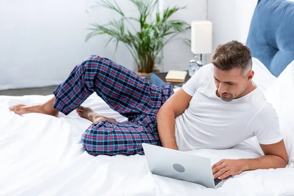 Enfoque selectivo del freelancer masculino que trabaja en la cama durante la mañana en casa - foto de stock