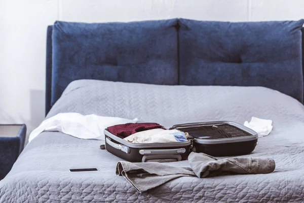 Enfoque selectivo de la bolsa de viaje, ropa y teléfono inteligente en la cama en casa - foto de stock