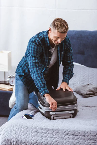 Щасливий дорослий чоловік упаковки дорожньої сумки в спальні вдома — стокове фото