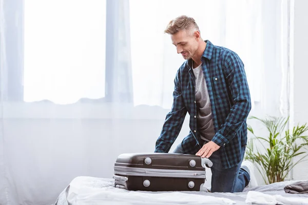 Alegre viajero masculino embalaje bolsa de viaje en el dormitorio en casa - foto de stock
