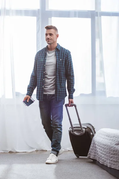 Hombre con pasaporte y billete de avión que lleva bolsa de viaje en casa - foto de stock