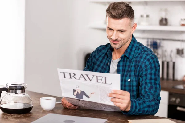Guapo sonriente hombre con camisa a cuadros leyendo el periódico de viaje por la mañana - foto de stock