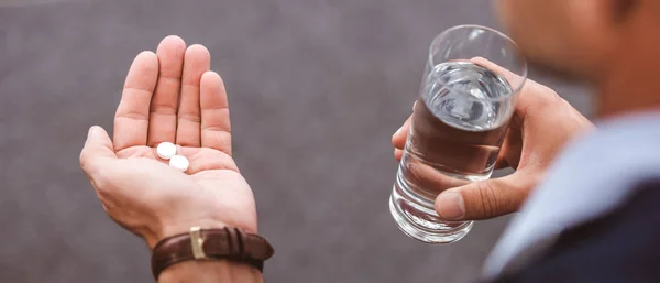 Vue partielle de l'homme d'affaires en costume tenant un verre d'eau et des pilules — Photo de stock