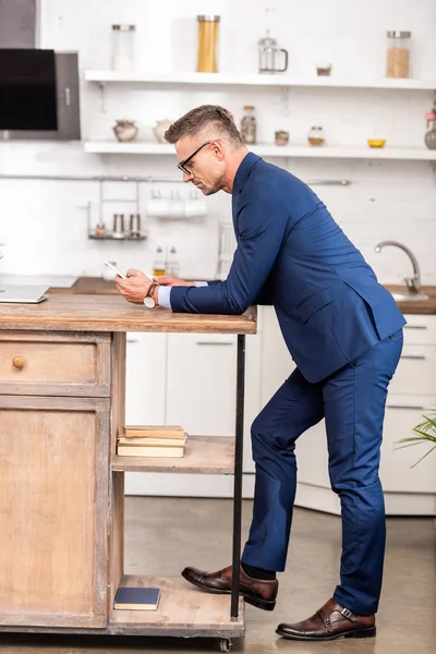 Side view of businessman leaning at table and using smartphone at home — Stock Photo