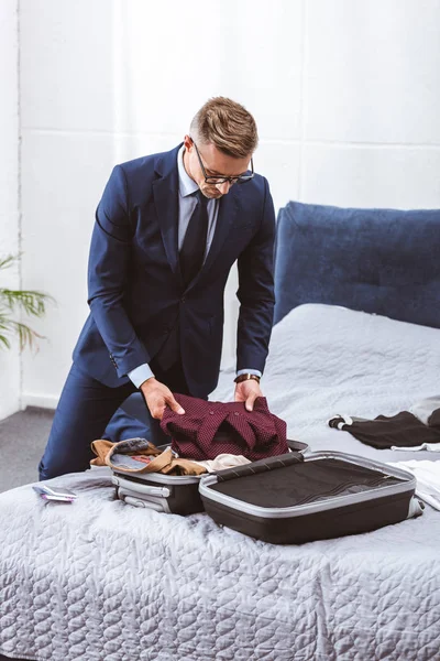 Hombre guapo en traje y gafas maleta de embalaje para viaje de negocios - foto de stock