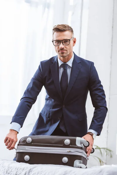 Schöner Geschäftsmann in Anzug und Brille, der Koffer packt und in die Kamera schaut — Stockfoto