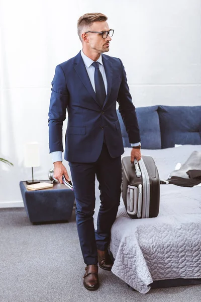 Hombre de negocios en ropa formal sosteniendo la maleta y mirando a casa - foto de stock