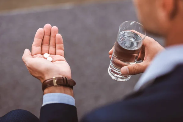 Colpo ritagliato di uomo d'affari in giacca e cravatta con bicchiere d'acqua e pillole — Foto stock