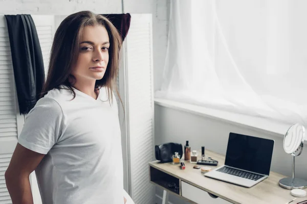 Retrato de cerca de una joven transgénero parada cerca del lugar de trabajo y mirando la cámara en casa - foto de stock