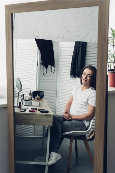 Ver a través de espejo reflexión joven transexual mujer mirando a la cámara en casa - foto de stock