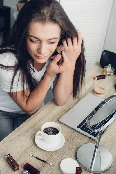 High angle view of young transgender woman with cup of coffee sitting at workplace at home and doing makeup — Stock Photo