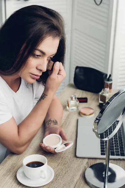 Serious young transgender woman doing makeup at workplace at home — Stock Photo