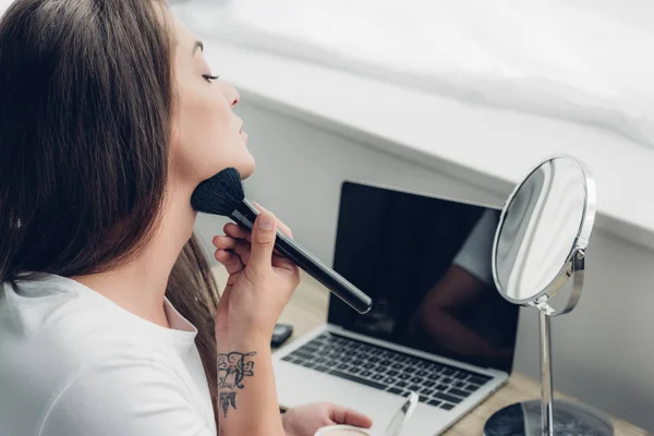 Joven mujer transgénero haciendo maquillaje con cepillo en el lugar de trabajo en casa - foto de stock