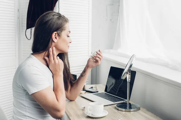 Joven mujer transgénero aplicando perfume en el cuello en el lugar de trabajo - foto de stock