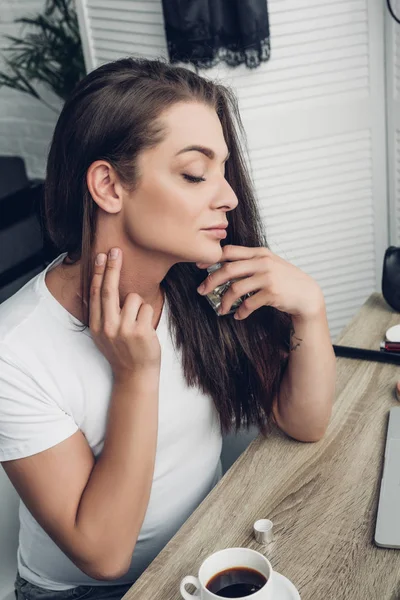 Close-up portrait of young transgender woman applying perfume on neck at home — Stock Photo