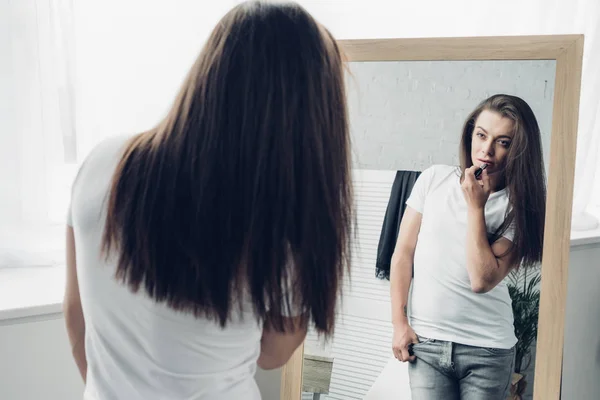 Junge Transgender-Frau trägt Lippenstift auf, während sie in den Spiegel schaut — Stockfoto