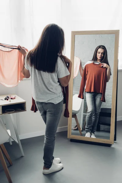Joven transexual mujer probándose camisas femeninas y mirando el espejo - foto de stock