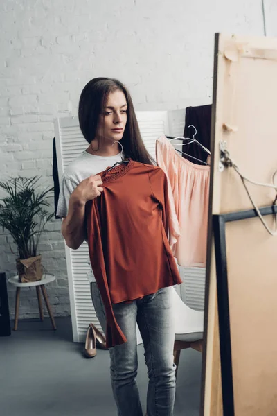 Young transgender woman trying on female shirts and looking at mirror at home — Stock Photo