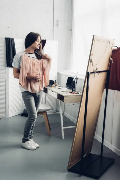 Mujer transgénero probándose la camisa femenina y mirando el espejo en casa - foto de stock