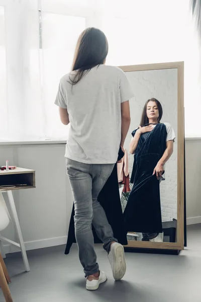 Молодая трансгендерная женщина с платьем смотрит на зеркало дома — стоковое фото