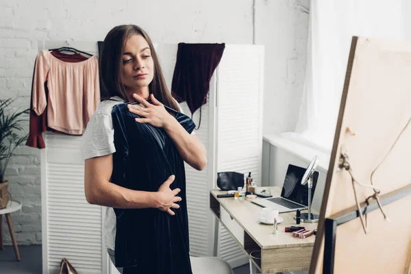 Трансгендерная женщина примеряет платье и смотрит в зеркало дома — стоковое фото