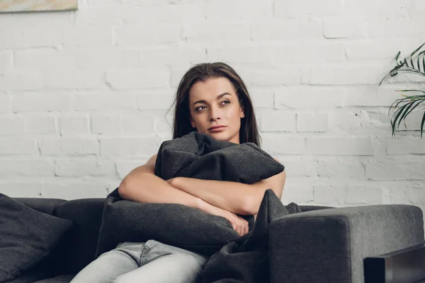 Thoughtful young transgender woman sitting on couch and looking away at home — Stock Photo