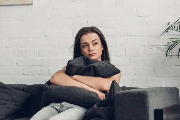 Réfléchie jeune femme transgenre assise sur le canapé et regardant loin à la maison — Photo de stock