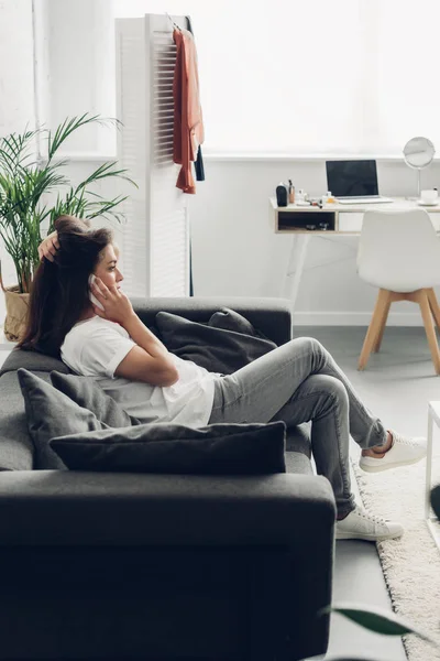 Вид збоку молода транссексуальна жінка розмовляє по телефону на дивані вдома — стокове фото
