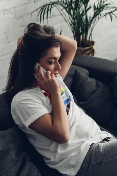 Молодая трансгендерная женщина разговаривает по телефону на диване дома — стоковое фото