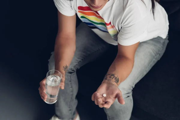 Cropped shot of young transgender woman with pill and glass of water sitting on couch — Stock Photo