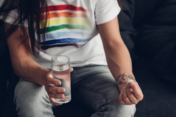 Cropped shot of man in t-shirt with pride flag holding glass of water and pill — Stock Photo