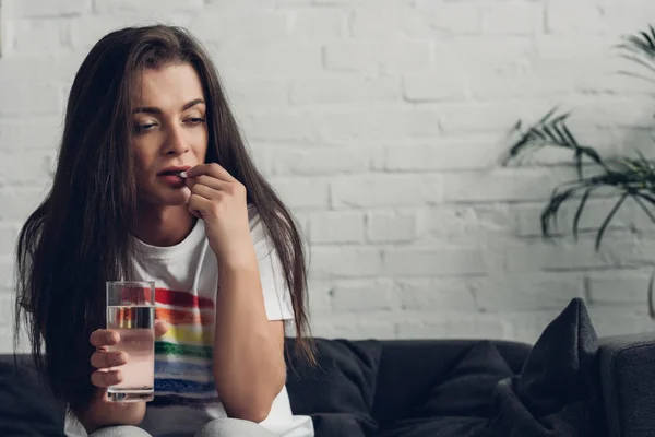 Пригнічена молода транссексуальна жінка приймає таблетки на дивані — стокове фото