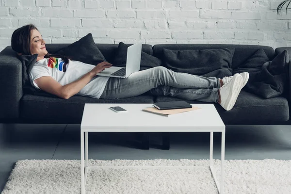 Розслаблена молода транссексуальна фрілансерка жінка працює з ноутбуком на дивані вдома — стокове фото