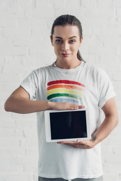 Junge Transgender-Frau im weißen T-Shirt mit Stolzfahne, Tablet mit leerem Bildschirm vor weißer Backsteinwand — Stockfoto