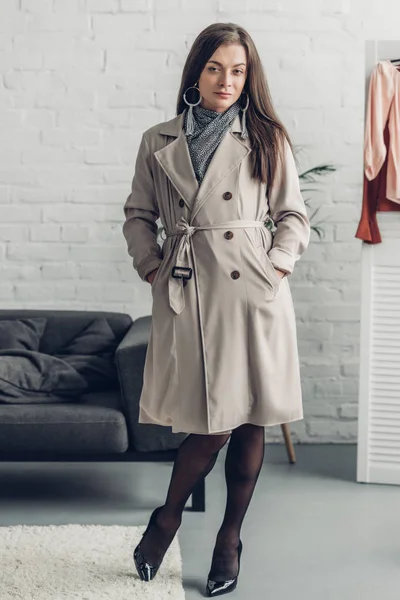 Jeune femme transgenre en trench coat regardant la caméra à la maison — Photo de stock