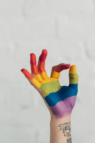 Обрізаний знімок руки, пофарбований у кольори прапора гордості, що показує добре жест перед білою цегляною стіною — стокове фото