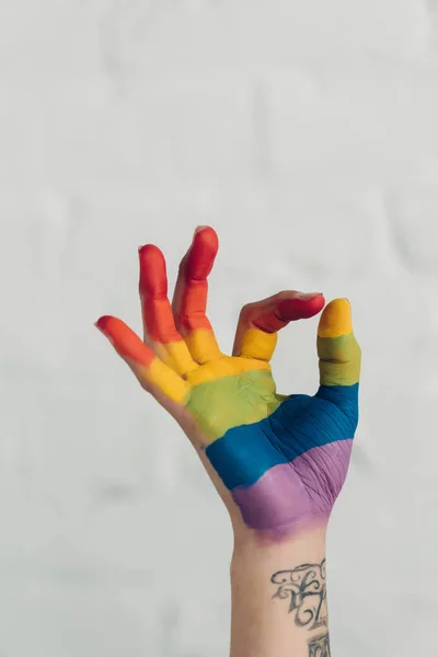 Recortado tiro de mano pintado en colores de la bandera de orgullo mostrando gesto bien delante de la pared de ladrillo blanco - foto de stock