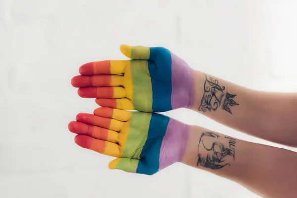 Recortado tiro de manos pintadas en colores de la bandera del orgullo en frente de la pared de ladrillo blanco - foto de stock