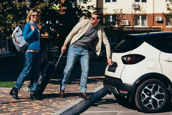 Coppia di turisti con zaino e bagaglio auto apribile in strada — Foto stock