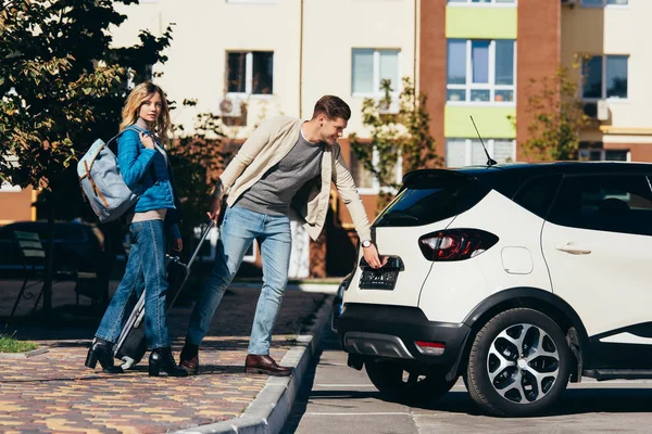 Couple of tourists with backpack and baggage opening car on street — Stock Photo