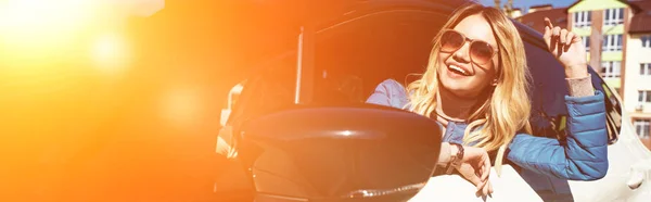 Cheerful young woman in sunglasses leaning out car on street — Stock Photo