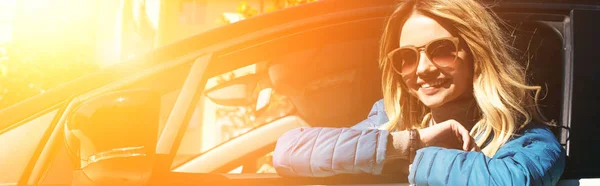 Cheerful young woman in sunglasses leaning out car on street — Stock Photo