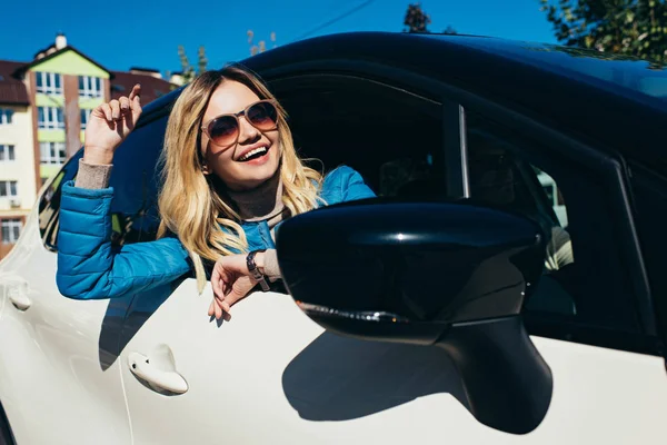 Портрет веселой молодой женщины в солнцезащитных очках, наклоняющейся к машине на улице — стоковое фото