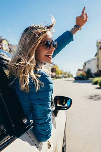 Cheerful young woman in sunglasses leaning out car on street — Stock Photo