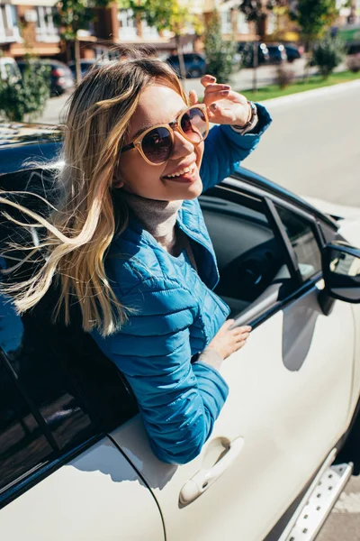 Весела молода жінка в сонцезахисних окулярах, що витісняє машину на вулиці — стокове фото