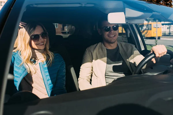 Smiling couple of tourists in sunglasses driving car while traveling together — Stock Photo