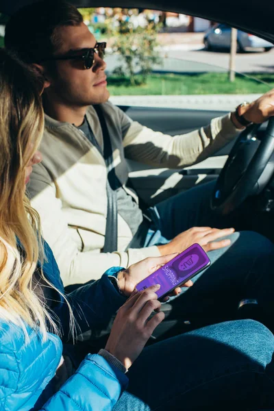 Mujer usando el teléfono inteligente con letras de compras en la pantalla mientras el marido conduce el coche - foto de stock