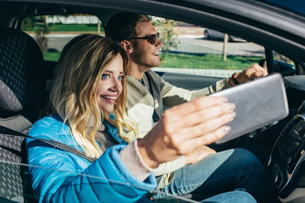 Smiling woman taking selfie together with boyfriend in car during trip — Stock Photo