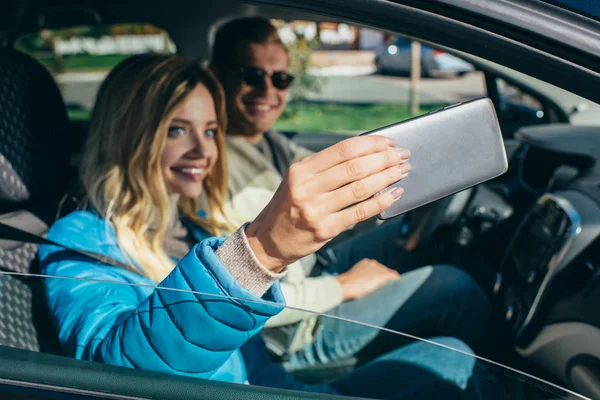 Sonriente mujer tomando selfie junto con novio en coche durante viaje - foto de stock